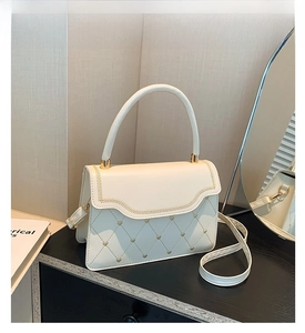 Detail of white quilted crossbody bag with golden heart studs and chain trim
