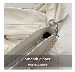 Detail of white leather shoulder bag featuring smooth silver zipper and large pearl chain