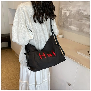 Detail of black canvas tote bag with red embroidered Hai letters on model in minimalist room