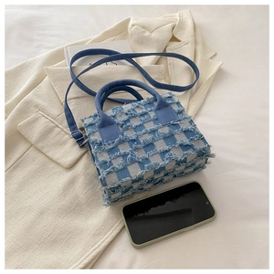 Detail der blau-weiß karierten Handtasche mit Vintage-Fransen und robuster Denim-Textur