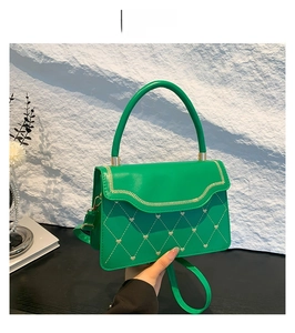 Detail of green quilted bag with heart stitching and wave edge flap on rock background