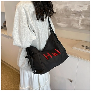 Detail of black nylon tote bag featuring bold red Hai embroidery and wide adjustable strap