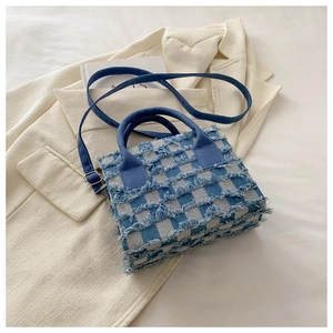 Detail der blauen Karo-Tragetasche mit Fransen auf beigem Blazer-Hintergrund