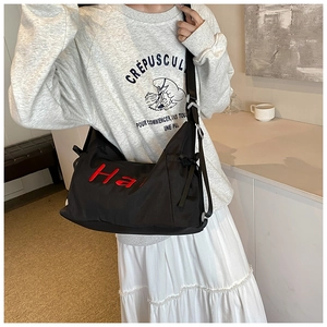 Close-up of black nylon travel bag with red Ha embroidery on a casual model