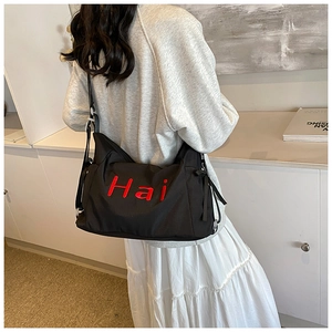 Detail of black canvas tote bag with red Hai lettering worn as a crossbody messenger