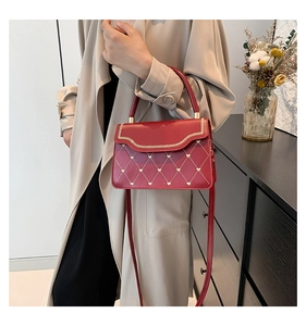 Detail of red quilted crossbody bag with heart embroidery and wavy edge on a shoulder
