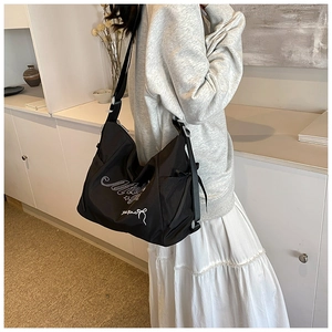 Detailed embroidery of Mickey lettering on black canvas messenger bag worn by a model