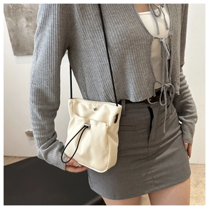 Detailed close-up of a minimalist cream crossbody phone bag with black drawstring closure