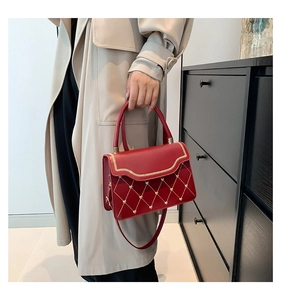 Detail of red quilted crossbody bag with golden heart hardware and curved trim