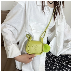 Détail du sac selle vert avocat avec motif en relief et breloque pompon en fourrure