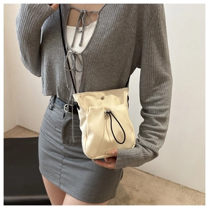 Detailweergave van de crème crossbody telefoontas met trekkoord en dunne zwarte riem