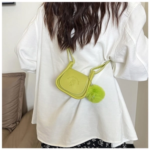 Détail du sac de selle vert avec motif gaufré et pendentif en peluche porté à l'épaule