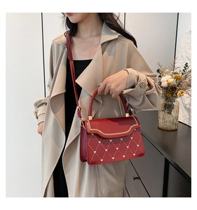 Detail of red heart-quilted crossbody bag with gold woven chain trim on a model