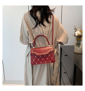 Detail of red quilted crossbody bag featuring gold wavy trim and small heart embroidery