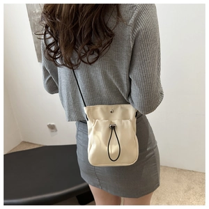 Detail of minimalist beige drawstring crossbody bag with soft faux leather texture