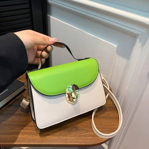 Minimalist white and green crossbody bag with gold round metal lock on a wooden table