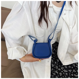 Dettaglio di una micro borsa a sella blu lucida con tracolla annodata alla moda