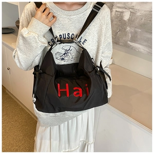 Detail of black tote bag with red Hai embroidery worn by a model in casual style