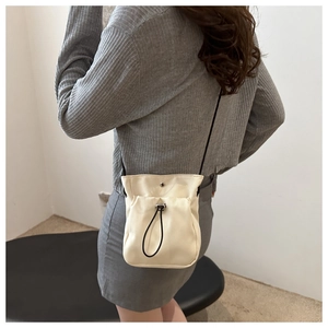 Detailopname van een crèmekleurige mini-crossbodytas met trekkoord gedragen door model