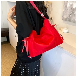 Detail of red crossbody bag featuring embossed lettering and a side bow decoration