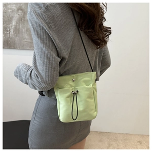 Detail of the light green canvas phone bag showing the silver snap and black drawstring