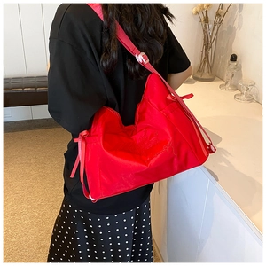 Detail of red nylon shoulder bag featuring embroidery, bow accent and wide strap