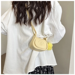 Vue détaillée du sac besace crème avec gaufrage dessin animé et pompon jaune doux
