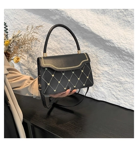 Detail of black quilted crossbody bag with golden heart accents and wavy embroidery