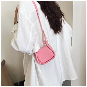 Dettaglio di una mini borsa a sella rosa indossata a tracolla su una camicia bianca