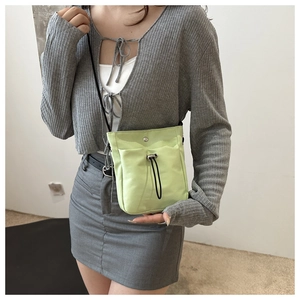 Close-up of a light green drawstring crossbody bag in durable nylon on a model