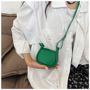 Dettaglio di una mini borsa a sella verde a tracolla indossata con un outfit primaverile