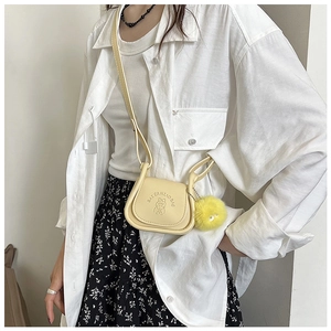 Détail du sac de selle en cuir beige avec gaufrage dessin animé et pompon jaune