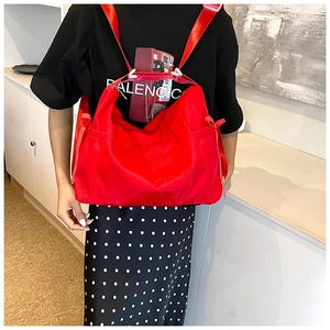 Close-up of red nylon tote bag featuring artistic embroidery and wide woven strap details