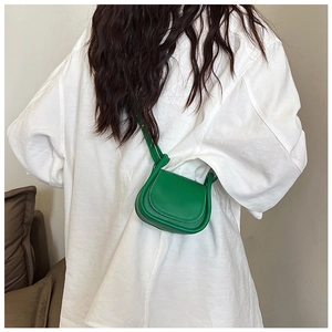Dettaglio mini borsa a sella verde con un particolare nodo sulla tracolla sottile