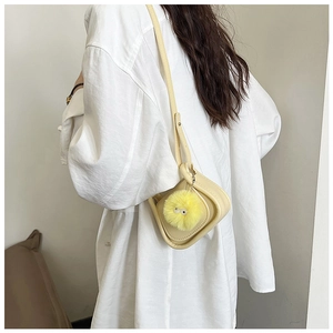 Détail d'un sac besace jaune crème avec un charmant pompon en peluche jaune à yeux