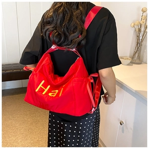 Detail of red nylon tote bag with yellow Hai embroidery and side drawstring adjustment