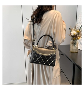 Detail of black quilted leather handbag with gold heart accent and wavy stitching