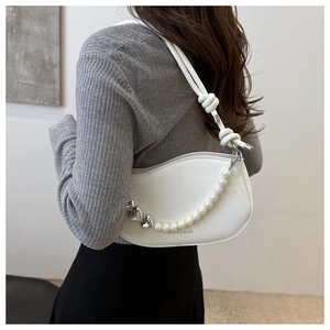 Detail of white leather hobo bag featuring pearl and silver heart charms with knotted strap