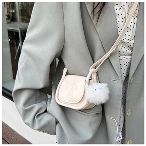 Mini sac crème bandoulière avec gaufrage cartoon et pompon porté sur une veste chic