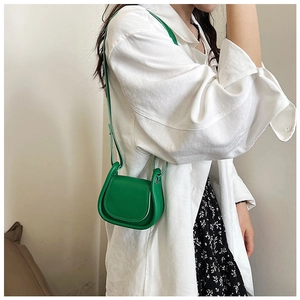 Dettaglio di una mini borsa a sella in pelle verde brillante indossata da una modella