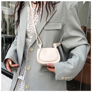 Dettaglio di una mini borsa a tracolla crema indossata con blazer grigio e vestito