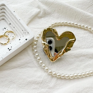 Detail eines goldenen Herz-Handyhalters mit gewelltem Metallrand und Spiegelfläche