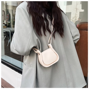 Vista posteriore di una modella con mini borsa a sella color crema in ecopelle liscia
