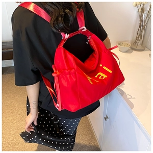 Detail of red nylon tote bag with yellow KAI embroidery shown on model in studio