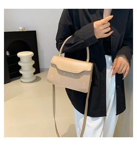 Detail of beige quilted crossbody bag with heart studs held by a model in a minimalist room