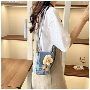 Détail d'un petit sac bandoulière bleu clair à fleurs porté par un mannequin
