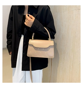 Detail of beige quilted crossbody bag with heart embroidery worn by a model