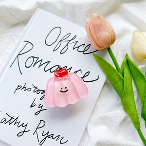 Close-up of pink pudding hair claw with cherry decor and smiley face on an art book