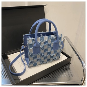 Detail der blau-weiß karierten Denim-Tasche mit modischen Fransenrändern und runden Griffen