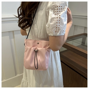 Roze nylon bucket bag met trekkoord gedragen door model in een witte kanten jurk